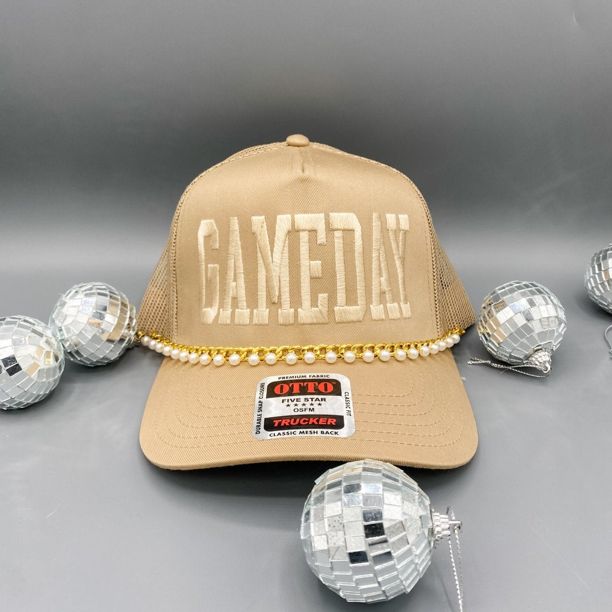 Beige cap with 'GAMEDAY' text and pearl embellishments on a gray background with disco balls.